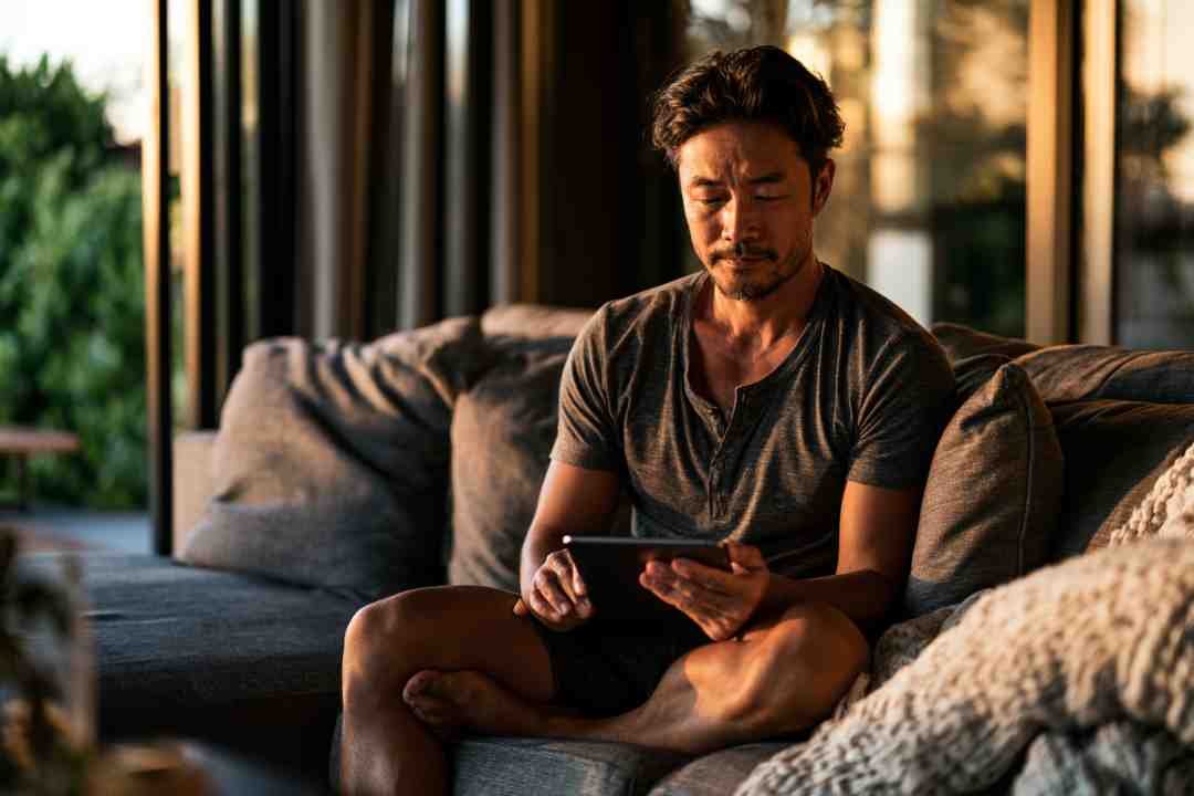 A man relaxing on a couch at golden hour, looking at a tablet